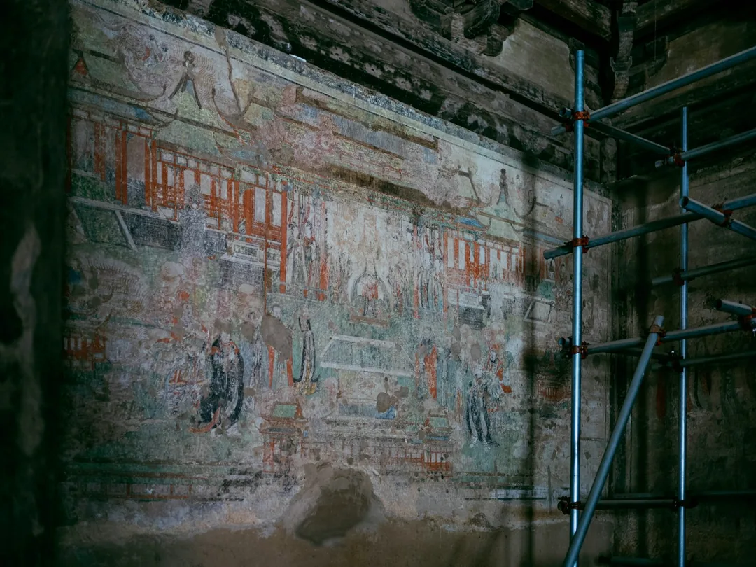 Pintura mural antigua sobre un muro deteriorado, con un andamio metálico montado delante para trabajar en altura